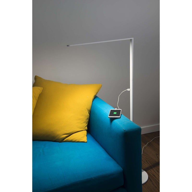 Matte white Lady 7 Floor lamp next to blue sofa with yellow pillow charging cell phone