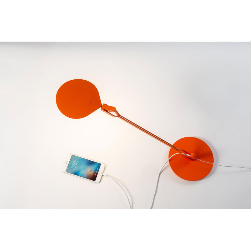 Splitty desk lamp in matte orange charging a mobile phone, Koncept lighting